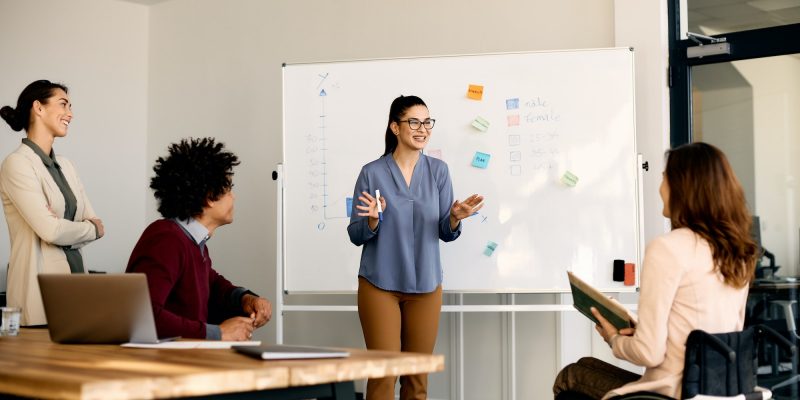 Young happy businesswoman giving presentation to group of her colleagues in meeting room.